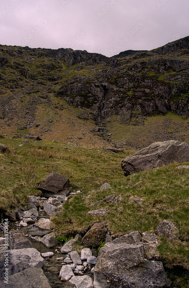 A giant rock wall with a narrow waterfall in the middle during a cloudy day