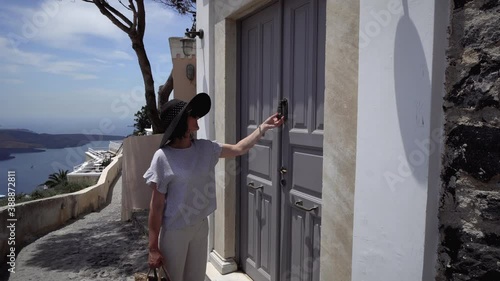 Woman visitor walk on Santorini street and knock on old door knocker