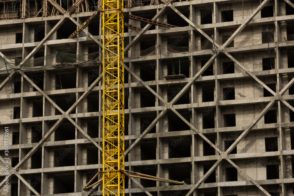 a concrete structure under construction for an apartment building. yellow tower crane goes up past the construction site of the house a concrete structure under construction for an apartment building. yellow tower crane goes up past the construction site of the house