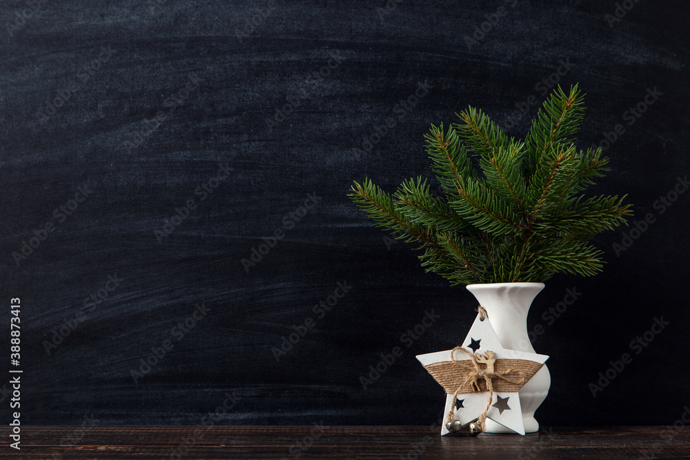 Fototapeta premium A vase with Christmas tree branches and a handmade star decoration against a chalkboard. The concept of a merry Christmas. Copy space.