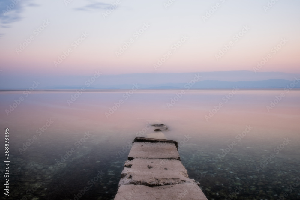 Stone pier with a boat in long exposure, low saturation. Croatia, Brac island, Supetar at sunrise. August 2020