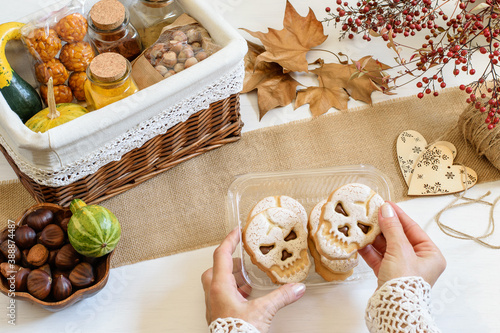 Female hands packing some Halloween presents: spices, chestnuts, pumpkins and scull biscuits. Care package, ethical idea, zero waste style life. photo