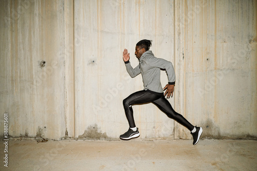 Solitary ethnic determined runner training along street in evening