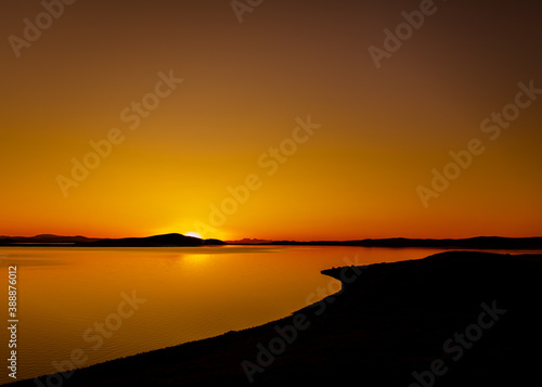 incredible landscape. Beautiful red-orange sunset, which is reflected in a huge lake, somewhere in the distance the outlines of the mountains are visible photo