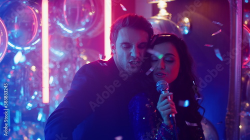 Energetic couple performing song in club. Woman holding microphone at party