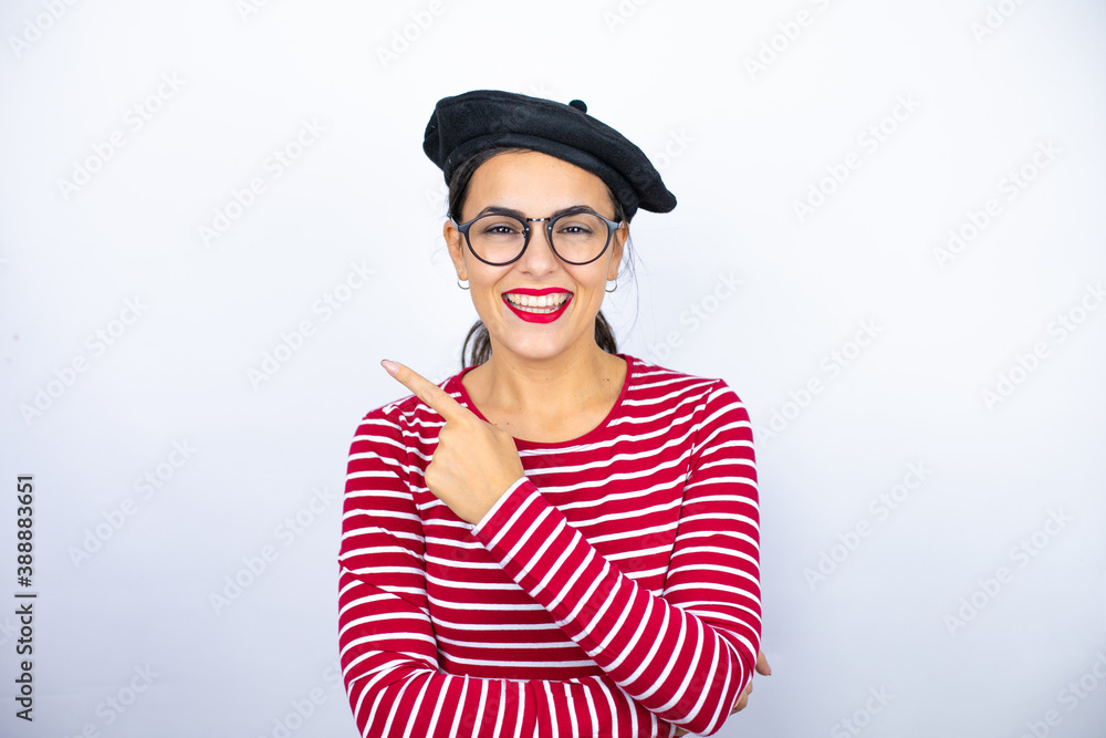 Young beautiful brunette woman wearing french beret and glasses over white background smiling and pointing with hand and finger to the side Young beautiful brunette woman wearing french beret and glasses over white background smiling and pointing with hand and finger to the side