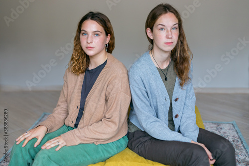 two similar girls are equally sitting on a yellow sofa photo