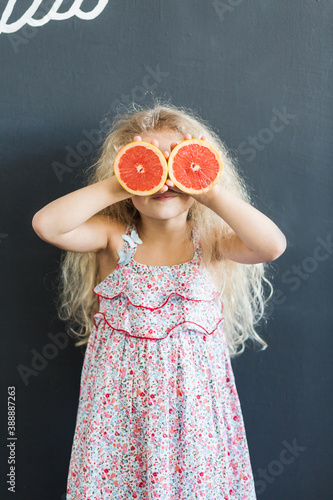 A little girl with curly hair holds grapefruit halves in her hands photo