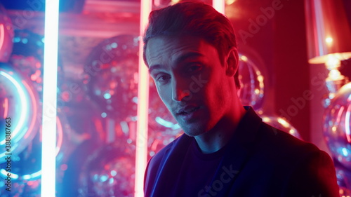 Affectionate guy smiling on neon lights background. Man winking at party