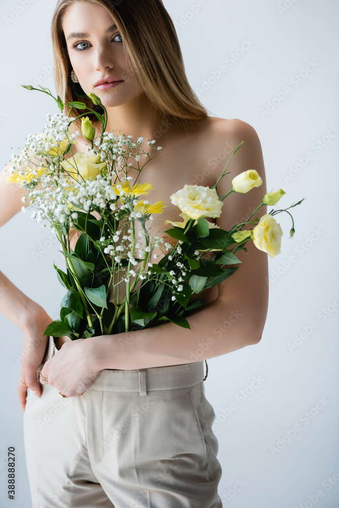 young woman with flowers in pants looking at camera while posing on white