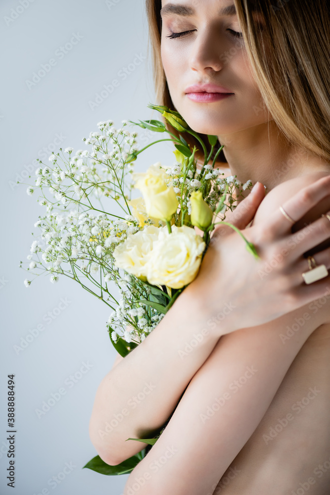 young model with closed eyes embracing flowers on grey