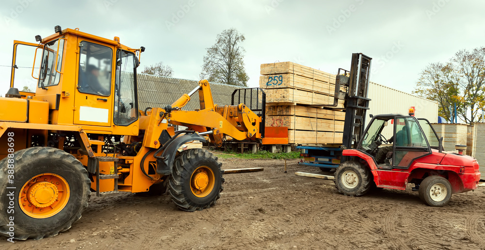 Two tractors load boards, lumber from the finished product warehouse into the container of the truck
