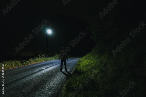 A sinister hooded figure, looking at a street light at night photo