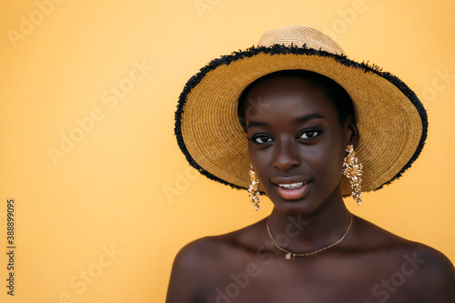 Young woman wearing hat smiling while standing against yellow wall photo