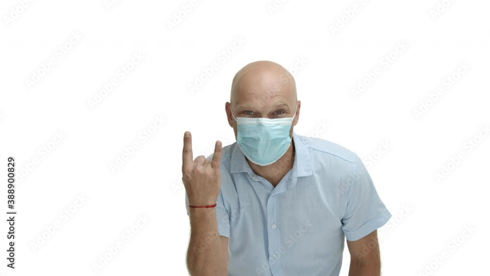 Quarantine, coronavirus and social distancing concept. Cheerful middle-aged bald man with blue eyes, wearing blue shirt and medical mask, showing rock-on gesture, having fun, white background Quarantine, coronavirus and social distancing concept. Cheerful middle-aged bald man with blue eyes, wearing blue shirt and medical mask, showing rock-on gesture, having fun, white background