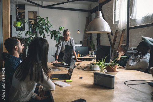 Businesswoman discussing with colleagues while standing by table at workplace photo