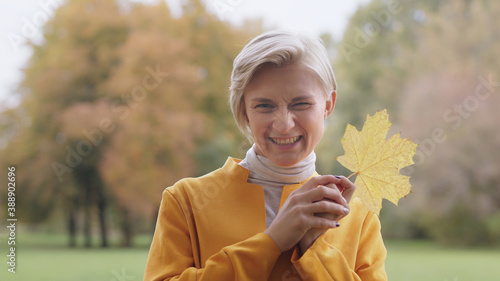 Young blond caucasian woman holding yellow autumn leaf in park. High quality photo