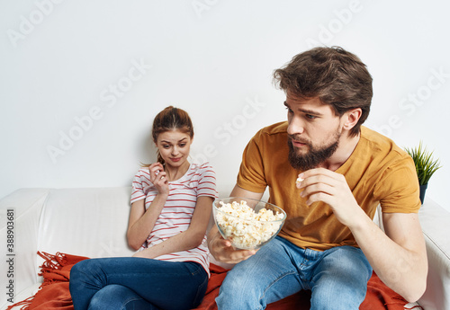 Man and pretty woman are sitting on the couch in front of the TV family friends flower in a pot