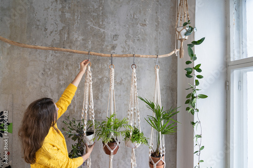 Woman gardener holding macrame plant hanger with houseplant over grey wall. Hobby, love of plants, home decoration concept. 