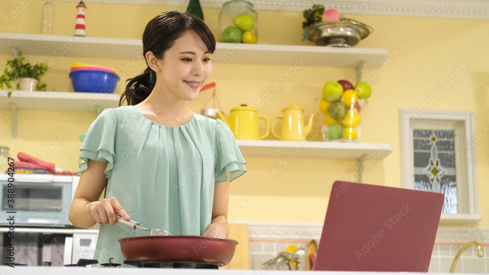 パソコンを見ながら料理をする女性