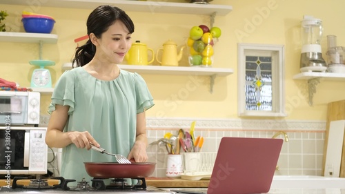 パソコンを見ながら料理をする女性
