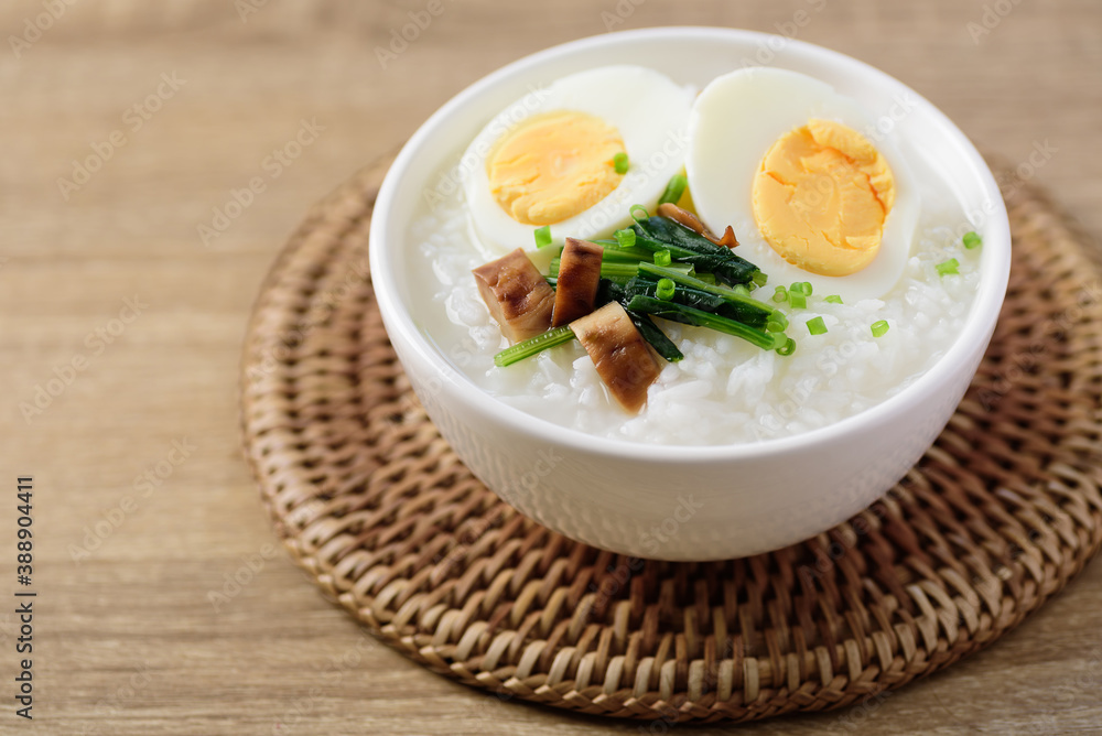 Asian food, Rice soup with boiled egg, grilled mushroom and spinach in a bowl on woven rattan sheet Asian food, Rice soup with boiled egg, grilled mushroom and spinach in a bowl on woven rattan sheet