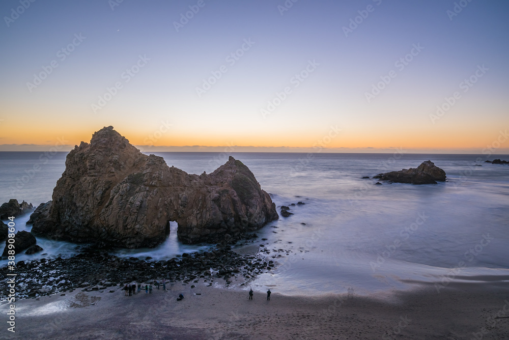Long exposure image of people watching the sunset in the famous Pfeiffer Beach and the Keyhole Arch.
