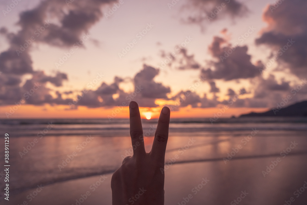 Woman hand do peace out with sunset beach.