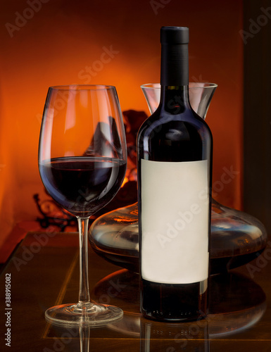 Bottle of red wine with decanter on a table and a fireplace behind