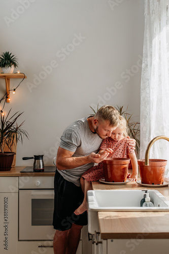 A happy little girl and a man sow seeds of domestic plants. Father and daughter at home in the kitchen. Plant care.
