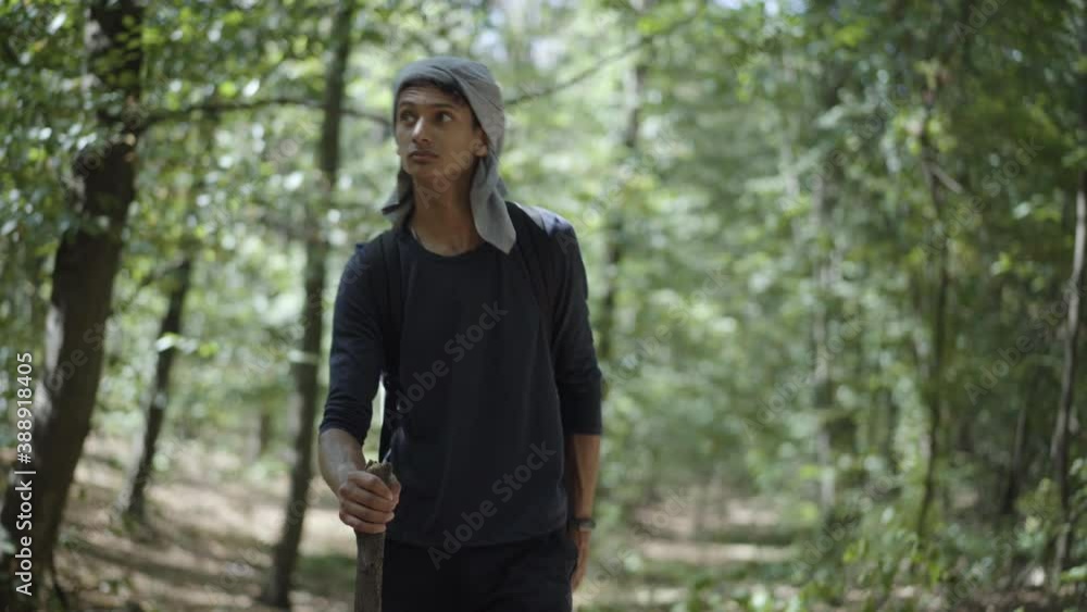 Portrait of male Gypsy walking in sunlight in forest. Young homeless man strolling with wooden stick outdoors on sunny summer day. Migration and homelessness concept. Portrait of male Gypsy walking in sunlight in forest. Young homeless man strolling with wooden stick outdoors on sunny summer day. Migration and homelessness concept.
