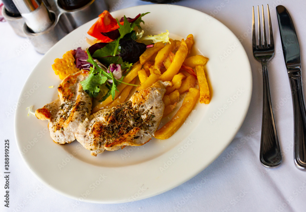 Spiced herb baked chicken fillet with side dish of crispy fries and vegetables