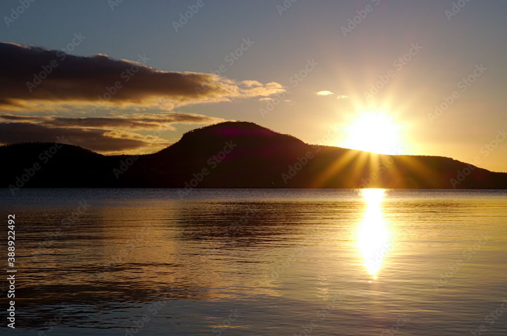 湖を照らす太陽。湖面に反射する太陽の光と空。屈斜路湖、北海道、日本。