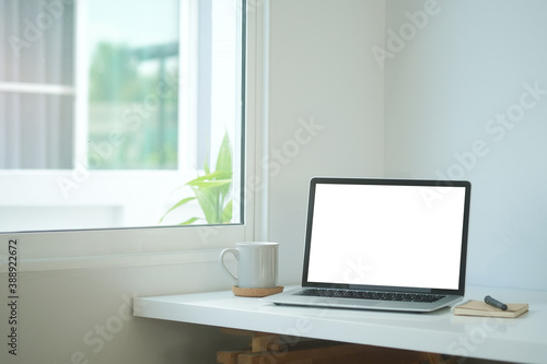 Simple workspace with white screen laptop, coffee cup and notebook on white table.