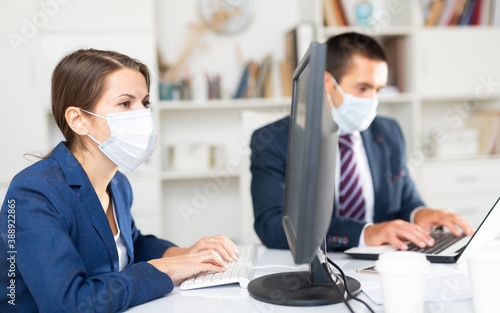 Portrait of young business woman focused on work with male colleague in office. People wearing medical face masks to prevent spread of viral infection