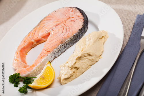 Dish of tasty steak of low-fried salmon served with hummus on plate