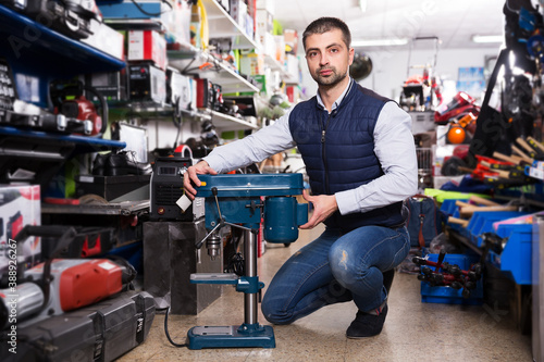 Positive man is choosing new puncher in tools store