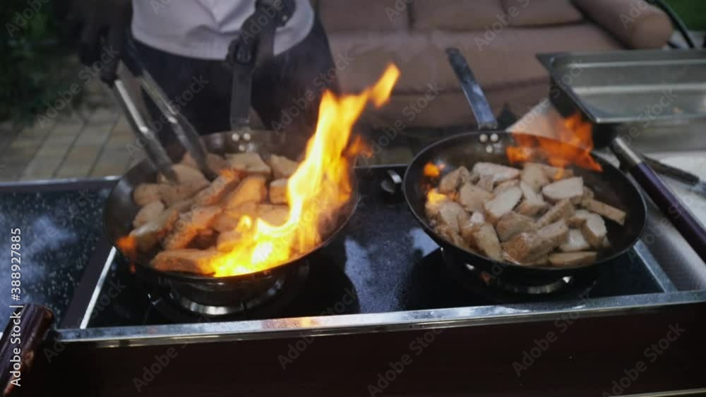 Chef cooks meat on an open fire in a burning pan outdoors in slow motion Chef cooks meat on an open fire in a burning pan outdoors in slow motion