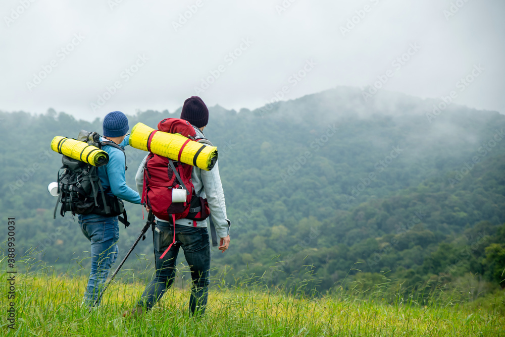 Portrait of Two Asian man friends with backpack hiking together on grass hill in autumn. Male backpacker relax and enjoy walking on mountain trail. Healthy outdoor lifestyle holiday vacation concept.
