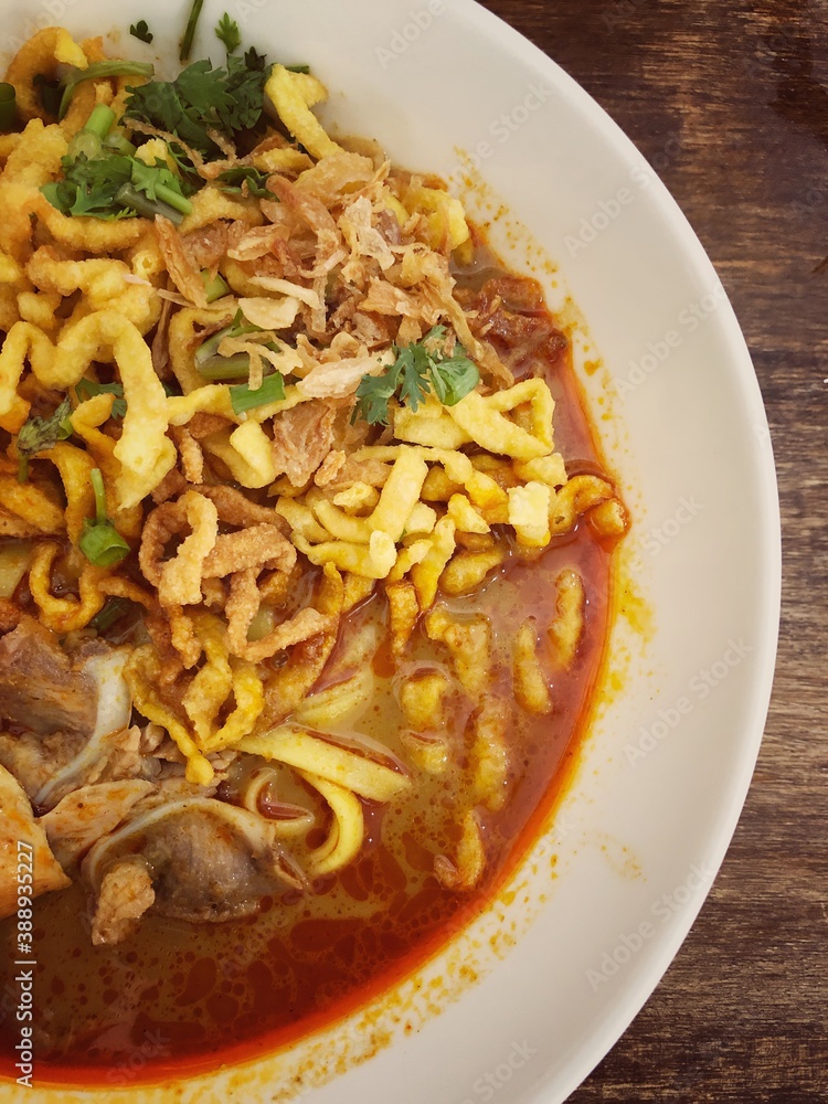 Khao Soi Kai, Thai spicy food in white blow on wooden table, Thai spicy soup. Thai Food. Northern Thai Style Curried Noodle Soup with Chicken Khao Soi Kai, Thai spicy food in white blow on wooden table, Thai spicy soup. Thai Food. Northern Thai Style Curried Noodle Soup with Chicken