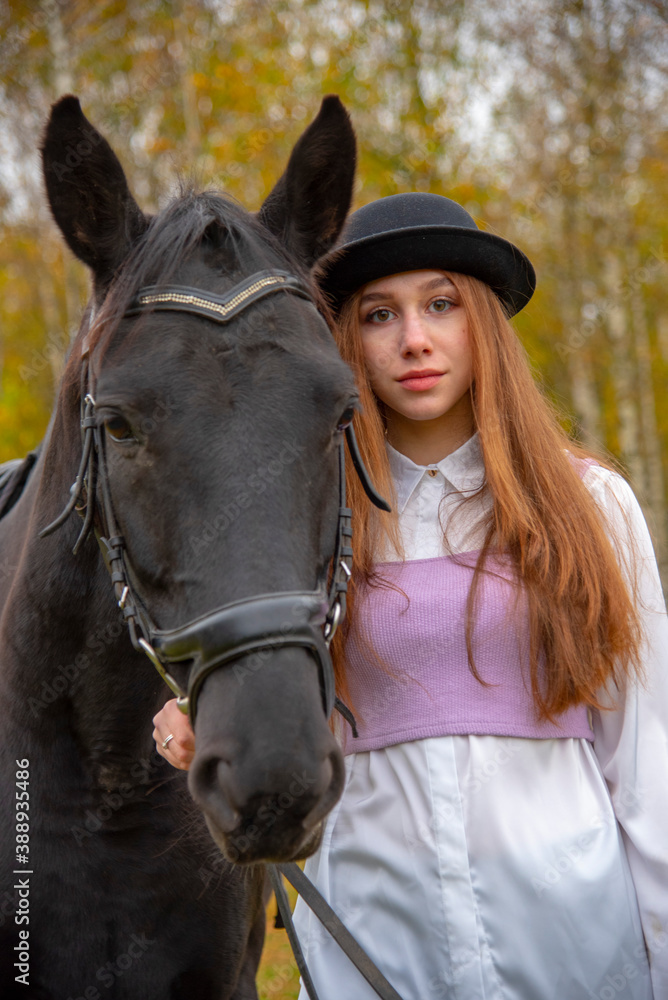 Obraz premium Red-haired girl in a black hat with a horse in the autumn forest.