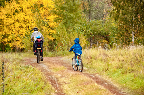 Family cycling in golden autumn park, active father and kids ride bikes, family sport and fitness outdoors 