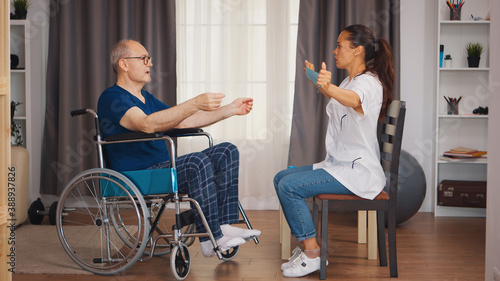 Senior man in wheelchair using resistance band during rehabilitation with help from doctor. Disabled handicapped old person with social worker in recovery support therapy physiotherapy healthcare