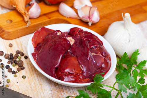 Raw chicken liver ready for cooking with fresh vegetables, greens and spices on wooden surface