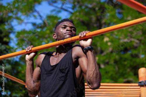 Close up of a slim black guy doing pulls up on a crossbar during workout in the park