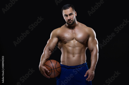 Front view portrait of an attractive sportsman holding a basketball with one hand isolated on black background