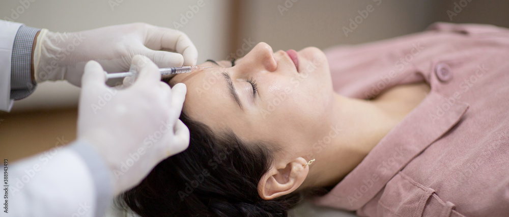 Young woman getting beauty facial injections in salon. Beautician makes cosmetic injection into the female patient face frown lines. Beauty injections, mesotherapy, revitalization and rejuvenation