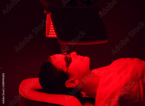 Young woman having red LED light facial therapy treatment in beauty salon. Beauty and wellness