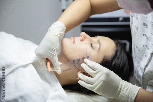 Therapist preparing female client for non-surgical cosmetic plasma lift- drawing and marking sections on her face with ruler. SMAS lifting. HUFU therapy- high intensity focused ultrasound procedure