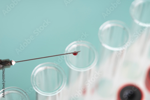 drop of blood on the tip of a syringe needle over glass test tubes over blue background